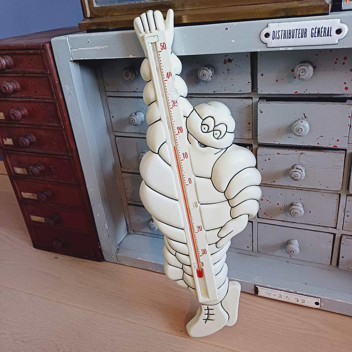 Thermomètre vintage en plastique représentant le personnage Bibendum Michelin, fabriqué par Bourbon, posé devant un meuble ancien.